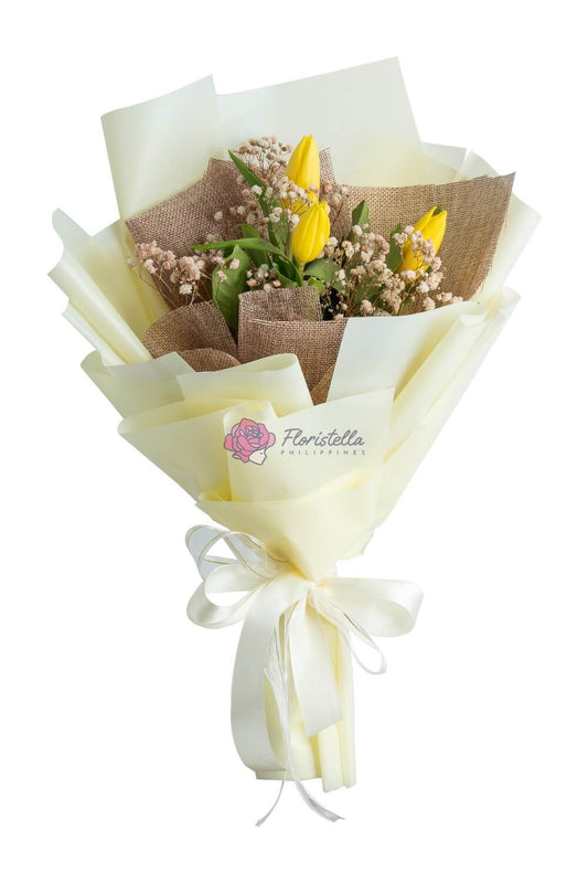 A bouquet of yellow tulips and gypsophila wrapped in brown and white paper with a ribbon, presented for delivery.